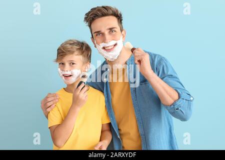 Père avec fils appliquant de la mousse de rasage sur leurs visages sur fond de couleur Banque D'Images