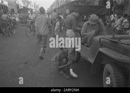 Photo Reportage Palembangs Deux soldats néerlandais, dont un deuxième lieutenant dans une jeep dans une rue commerçante de Palembangs. Un jeune homme avec un pied blessé vient mendier? Date: 1947 Lieu: Indonésie, Antilles Néerlandaises De L'Est Banque D'Images