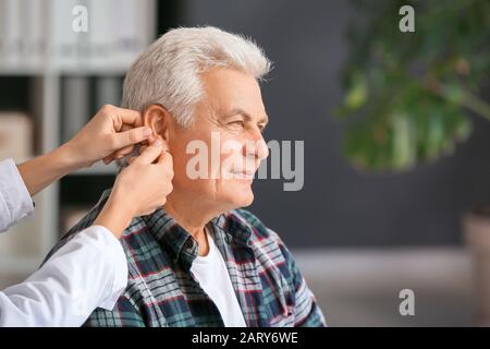 Médecin mettant l'aide auditive dans l'oreille de l'homme mûr en clinique Banque D'Images