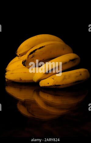 Image d'une main de bananes sur une table où les bananes sont reflétées avec un fond sombre. Style alimentaire sombre Banque D'Images