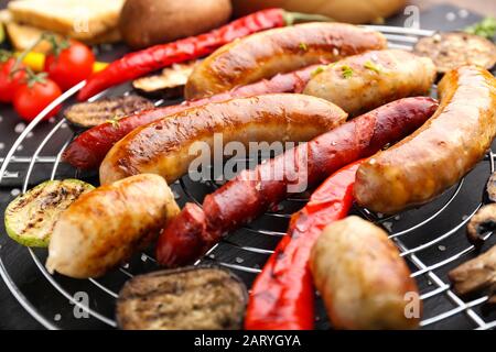 Saucisses grillées savoureuses avec légumes sur la grille, gros plan Banque D'Images