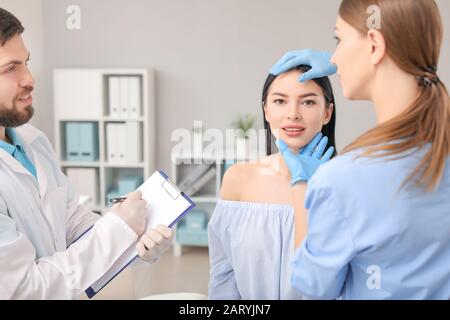 Chirurgien plastique avec assistant examinant le visage de la jeune femme avant l'opération en clinique Banque D'Images