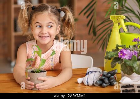 Bonne petite fille avec une jeune plante dans le pot à la maison Banque D'Images