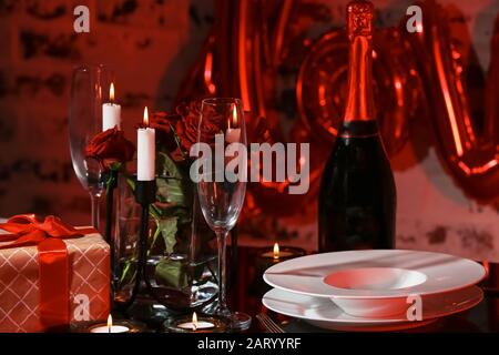 Champagne, fleurs, cadeau et assiettes sur table préparés pour un dîner romantique le jour de la Saint-Valentin Banque D'Images