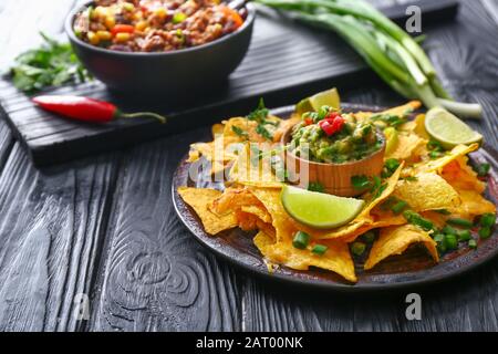 Assiette avec nachos savoureux et guacamole sur la table sombre Banque D'Images