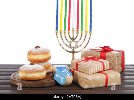 Menorah, cadeaux, beignets pour Hanoukkah et dreidel sur table contre fond blanc Banque D'Images