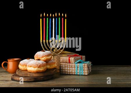 Menorah, beignets pour Hanoukkah et cadeaux sur table contre fond sombre Banque D'Images