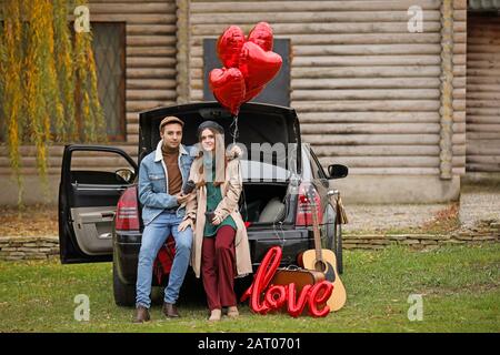 Un jeune couple heureux avec des ballons de voiture et d'air dans le parc. Célébration de la Saint-Valentin Banque D'Images