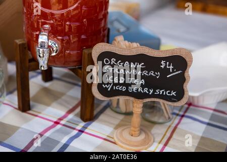 Signe noir écrit à la main indiquant les ingrédients d'un thé glacé. Stand de nourriture fermier avec grande carafe de thé glacé à la saveur de fraise Banque D'Images