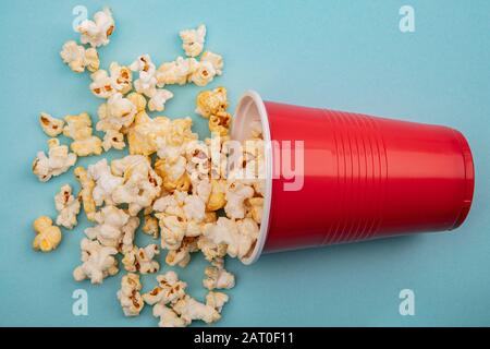 Craquement croquant du maïs-popcorn dans une tasse en plastique sur fond bleu vif Banque D'Images