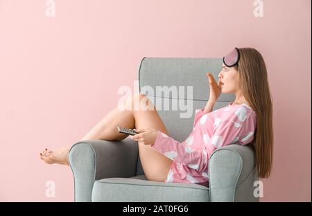 Une femme choquée qui regardait la télévision tout en s'asseoir dans un fauteuil sur fond de couleur Banque D'Images