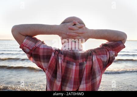 homme se tenant sur la plage et regardant l'éclairage au coucher du soleil. vue arrière pendant la soirée d'été Banque D'Images