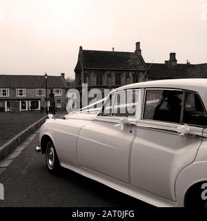 Une limousine avec chauffeur blanc attend un couple marié pour quitter l'église après leur cérémonie de mariage Banque D'Images