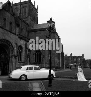 Un Bode et une salle de bains quittant l'église pour se marier avec leur chauffeur et leur voiture les attendant à l'extérieur Banque D'Images