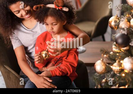 Heureuse femme afro-américaine et sa petite fille décorant arbre de Noël à la maison Banque D'Images