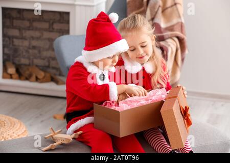 Mignons petits enfants en costumes de Santa et avec cadeau de Noël à la maison Banque D'Images