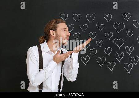 Bel homme qui souffle baiser sur fond sombre. Célébration de la Saint-Valentin Banque D'Images