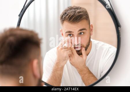 Jeune homme mettant dans des lentilles de contact près du miroir Banque D'Images