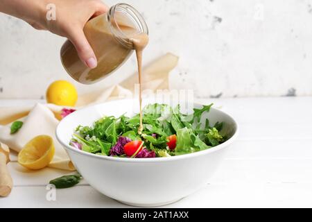 Femme qui verse de savoureux tahini du pot à la salade de légumes dans le bol Banque D'Images