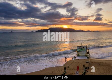 Nha Trang, le lever du soleil du Vietnam avec la mer de Chine méridionale, la mer de l'est, les îles éloignées et une épave de navire sur la plage de premier plan. Les gens font de l’exercice Banque D'Images