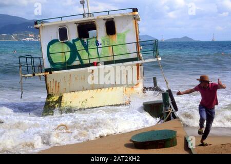 Un homme part des vagues à côté d'une barge abandonnée. En décembre 2019, une barge de ferry portant le numéro KH-98668-TS a glissé et a été lavée à la plage de Nha Trang dans la station balnéaire de Nha Trang au Vietnam, en Asie du Sud-est, Indochina, en Asie, et est encore bloquée sur le sable à l'est de la rue Tran Phu, Nha Trang, le 29 janvier 2020. Banque D'Images