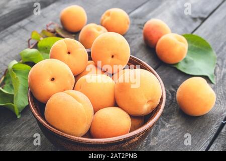 Délicieux abricots mûrs dans un bol à côté de feuilles vertes sur une table en bois. Gros plan. Banque D'Images