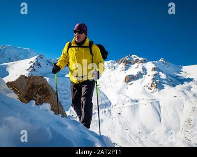 Un homme monte une montagne sur une pente enneigée. Un homme avec un sac à dos dans des lunettes de soleil et une veste chaude jaune. Beau temps dans les montagnes d'hiver Banque D'Images