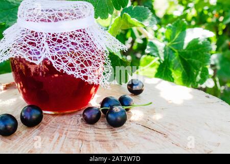 Confiture de cassis noir dans un bocal en verre sur une table en bois contre la bague de cassis dans le jardin. Confiture naturelle de groseilles. Gros plan. Banque D'Images