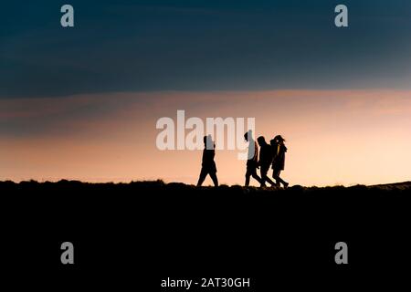 Un groupe d'amis marchant à la maison comme le soleil se couche à la fin de la journée. Banque D'Images