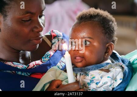 Mère avec sa fille baptisée et la bougie de baptême dans la chapelle du village stilt de Nzulezo, Ghana, Afrique Banque D'Images