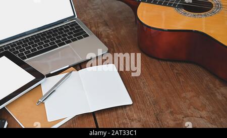 Table de travail de l'auteur-compositeur. Photo courte de note, crayon, guitare acoustique, tablette blanche à écran blanc et ordinateur portable tout cela met sur le bois de Banque D'Images