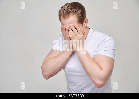 Un homme dans une chemise blanche crie couvrant son visage avec ses paumes. Le concept de dépression profonde. Gros plan. Banque D'Images