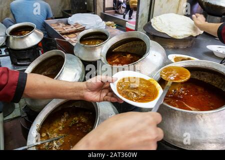 Un employé de restaurant qui butie un curry de mouton du grand pot dans l'un des restaurants de Chandni Chowk dans le Vieux Delhi Inde Banque D'Images