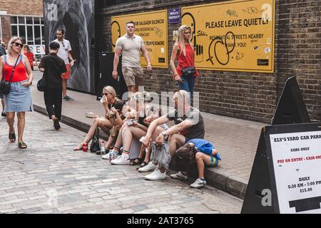 Londres/Royaume-Uni - 22/07/18: Mère, père, fille et 3 fils assis sur le côté d'une route à Ely's Yard au dimanche haut de gamme, l'un des 5 marchés Truman, Banque D'Images