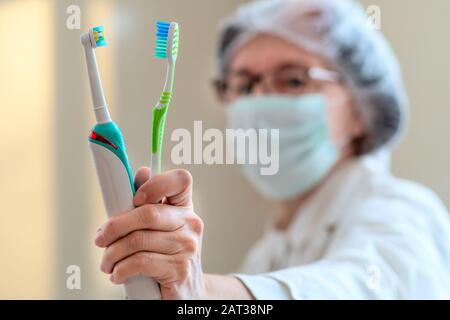 Médecin Dentiste tient deux brosses à dents dans sa main, électrique et classique. Vue en gros plan. L'équipement dentaire. La médecine, les soins de concept. Banque D'Images