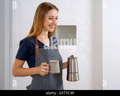 Heureuse et belle jeune blonde femme portant un tablier et servant du café. Banque D'Images