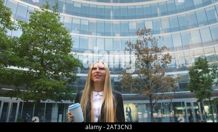 Par en dessous de la blonde woman in suit le café dans la tasse de papier à l'écart sur rue. Banque D'Images
