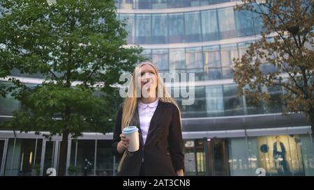 Par en dessous de la blonde woman in suit le café dans la tasse de papier à l'écart sur rue. Banque D'Images