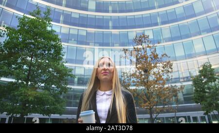 Par en dessous de la blonde woman in suit le café dans la tasse de papier à l'écart sur rue. Banque D'Images