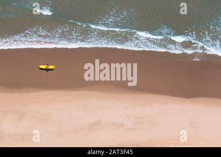 Vue aérienne d'une plage de sable (Praia Cordoama) au Portugal avec un surfeur et son panneau jaune en direction de l'eau. Concept de surf Banque D'Images
