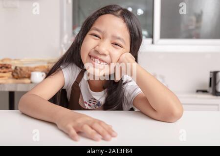 Une petite fille asiatique souriante a vu sa dent cassée sur une table de cuisson blanche dans la cuisine avec bonheur.