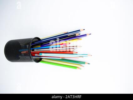 Divers types de crayons et crayons de cire placés dans un pot qui sont tombés sur un bureau blanc isolé Banque D'Images