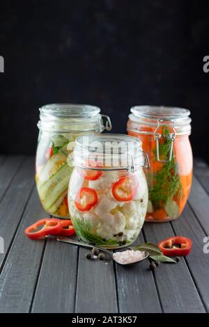 trois bocaux en verre de chou-fleur fermenté, concombres, carottes, piment, épices, sel. légumes sur fond sombre. la fermentation est une source o Banque D'Images