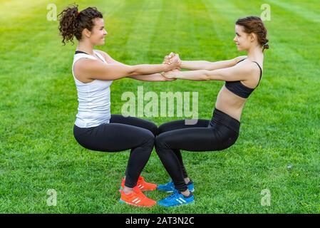 Séduisantes femmes heureux portant des vêtements de sport faisant des exercices tenant les mains et se croisant dans le stade Banque D'Images