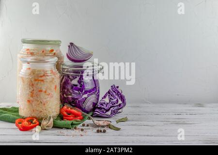 trois bocaux en verre de blanc fermenté, de chou rouge, d'oignons, de poivre, de légumes sur fond clair. à l'aide de vert textile. la fermentation est une source de p Banque D'Images