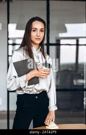 Jolie brunette avec des papiers dans elle et des tasses de café, travaillant dans le fonctionnaire Banque D'Images