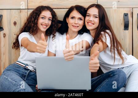 Une belle femme adulte et deux jeunes filles à la maison montre des pouces de classe vers le haut Banque D'Images