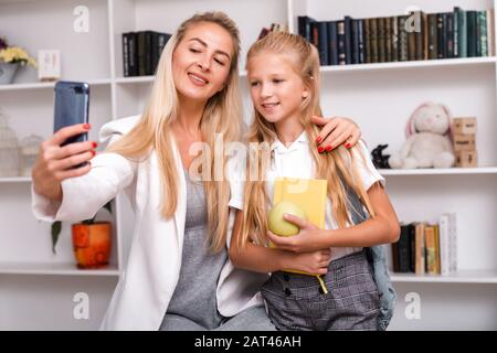 Jolie mère et petite fille avec un sac à dos et un livre dans ses mains, faisant des selfies à la maison Banque D'Images