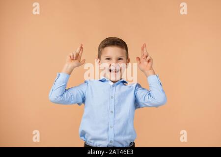 drôle petit garçon enfant en chemise bleue faisant un geste de pistolet sur fond beige. Banque D'Images