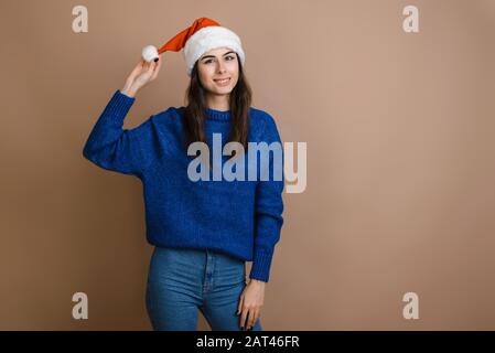 Belle fille dans Red Santa Claus chapeau sur fond brun regardant heureux et excité. Joyeux Noël et les vacances du nouvel an. Banque D'Images